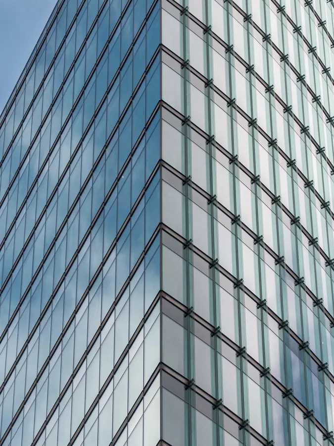 Fachada de vidro de um edifício alto refletindo céu e nuvens