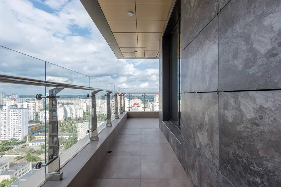Terraço com guarda-corpo de vidro e corrimão metálico, com a cidade ao fundo