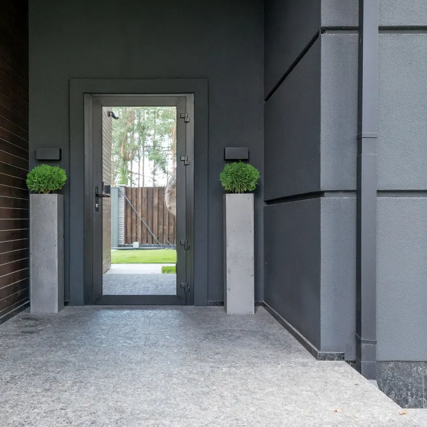 Entrada com porta de vidro emoldurada em perfil escuro, entre parede de madeira e parede cinza