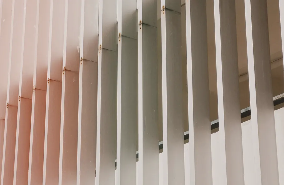 Lâminas verticais de alumínio claro em sequência, criando faixas de luz e sombra